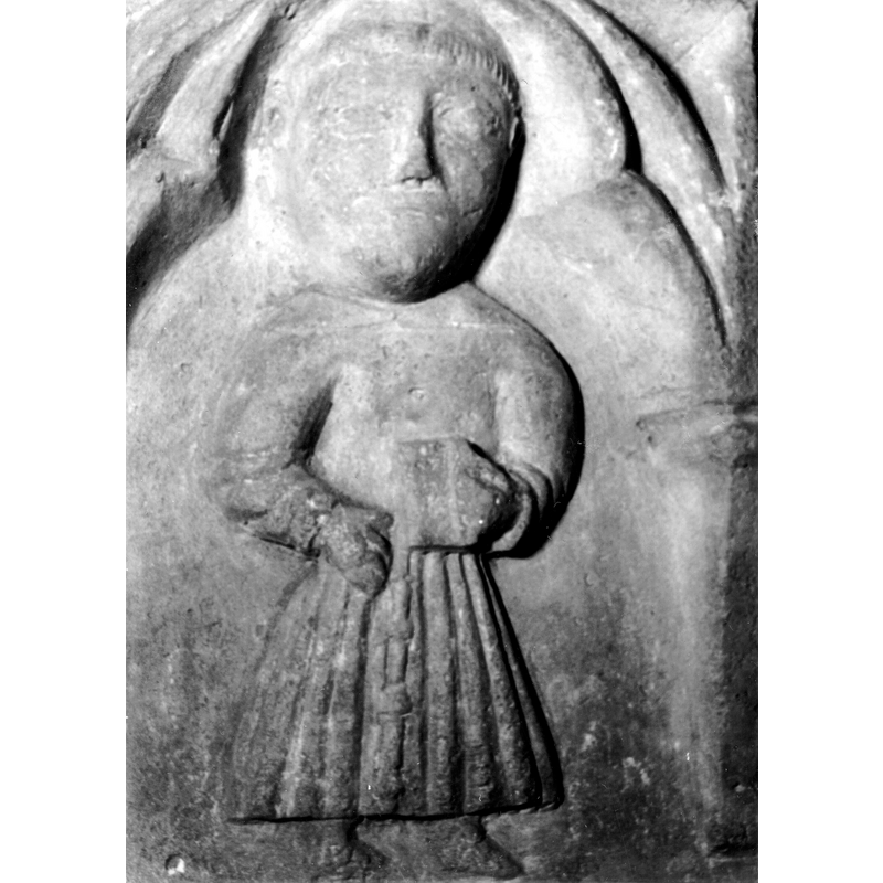 Sourca caption: "Detalle de una de las figuras de la parte superior de la pila bautismal gótica; se representa una figura, posiblemente un fraile franciscano, con un libro en las manos entre arquerías polilobuladas [...] pila bautismal de la iglesia de la Natividad de Hueto Arriba" [NB: not only is the figure tonsured but it is the only one that shows clearly the knotted cingulum characteristic fo the Franciscans]