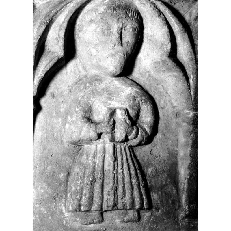 Source caption: "Detalle de una de las figuras de la parte superior de la pila bautismal gótica; se representa una figura, posiblemente un fraile franciscano, con un libro en las manos entre arquerías polilobuladas [...] pila bautismal de la iglesia de la Natividad de Hueto Arriba" [NB: not only is the figure tonsured but it is the only one that shows clearly the knotted cingulum characteristic fo the Franciscans]