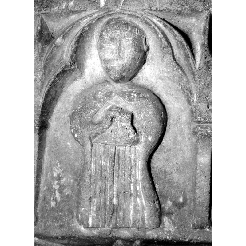 Source caption: "Detalle de la parte superior de la pila bautismal; presenta, entre arquerías polilobuladas, una figura humana que puede representar a un apóstol, un profeta o un fraile franciscano con libros o cartelas en las manos [...] pila bautismal de la iglesia de la Natividad de Hueto Arriba"