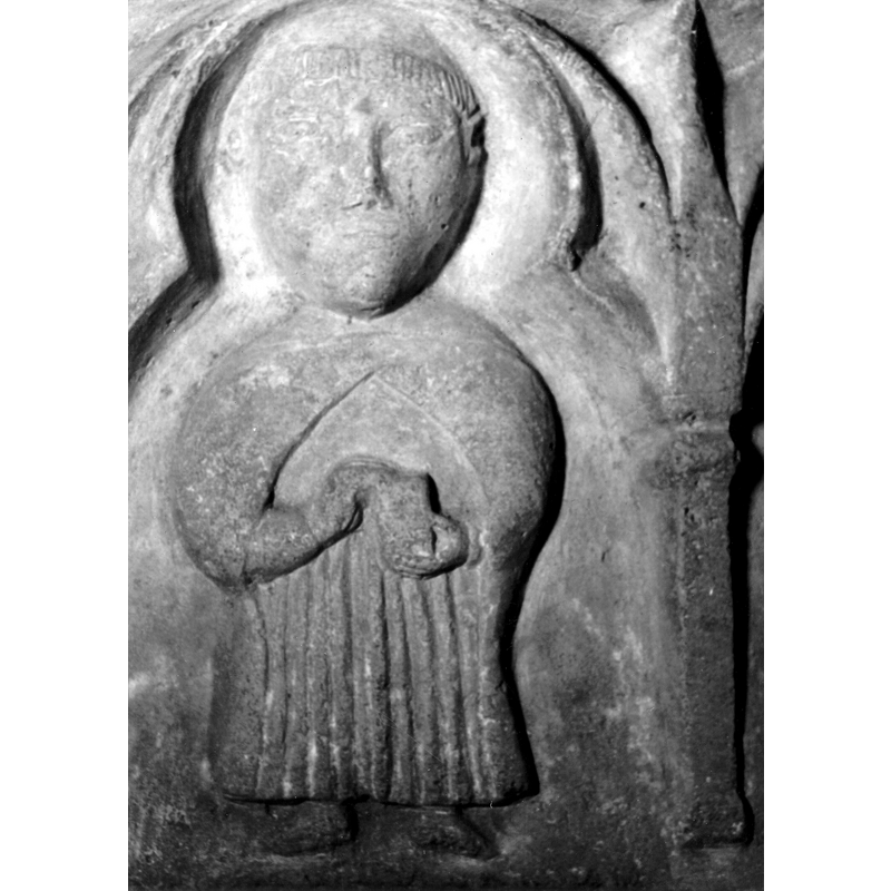 Source caption: "Detalle de la parte superior de la pila bautismal; presenta, entre arquerías polilobuladas, una figura humana que puede representar a un apóstol, un profeta o un fraile franciscano con libros o cartelas en las manos [...] pila bautismal de la iglesia de la Natividad de Hueto Arriba"