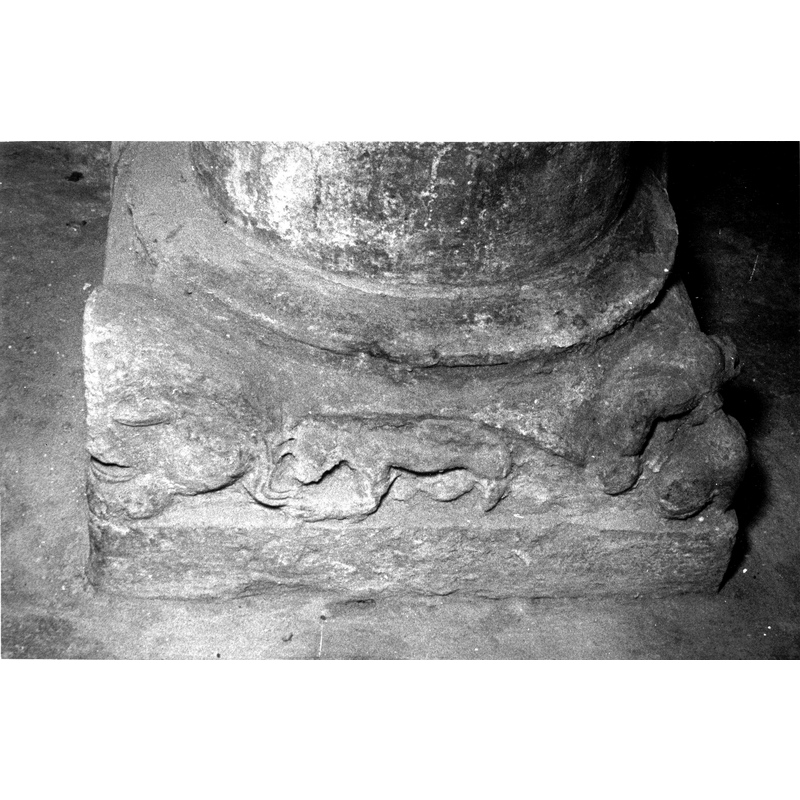Source caption: "Vista frontal de la basa de la pila bautismal; está decorada con cuatro mascarones y elementos vegetales geometrizados [...] pila bautismal de la iglesia de San Martín de Arlucea" [NB: the figure between the mascarons appears to be a quadruped passant to the left]