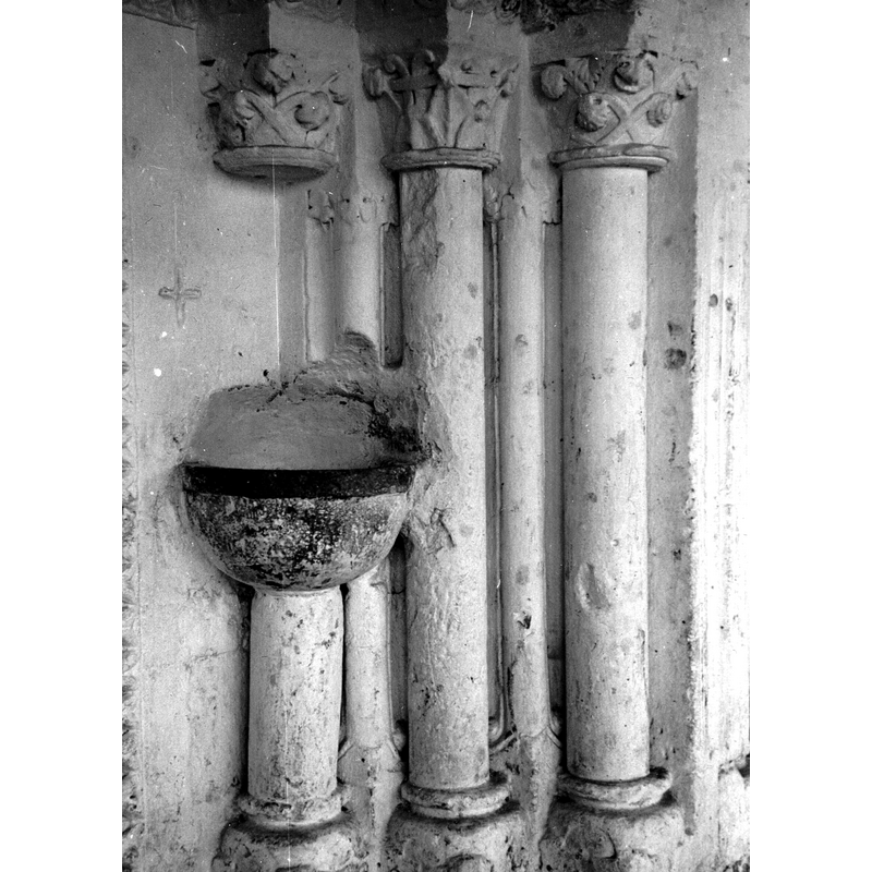 Source caption: "portada de la iglesia de San Julián y Santa Basilisa de Oreitia [...] Vista frontal de las tres columnas de la parte derecha de la portada; presentan fustes lisos, basas de garras y capiteles muy decorados con motivos vegetales. Una de los fustes ha sido partido para colocar una pila de agua bendita"