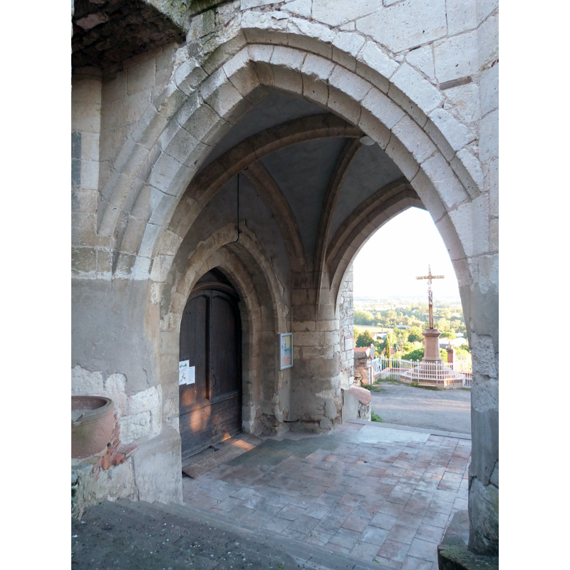Source caption: "Porche de l'église Saint-Barthélemy" -- the reddish vessel on the left, sitting on a stone ledge of the porch, is quite likely the remains of a baptismal font