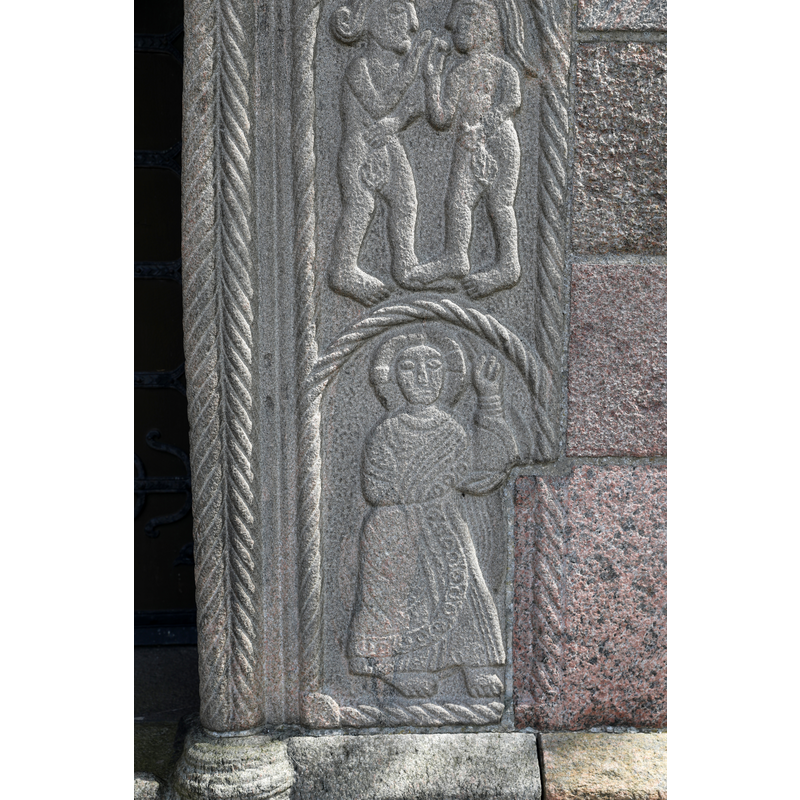 Adam and Eve facing each other, holding the fruit in their hands and holding leaves over their pudenda -- Christ's left hand blessing -- formerly the south portal of the medieval church