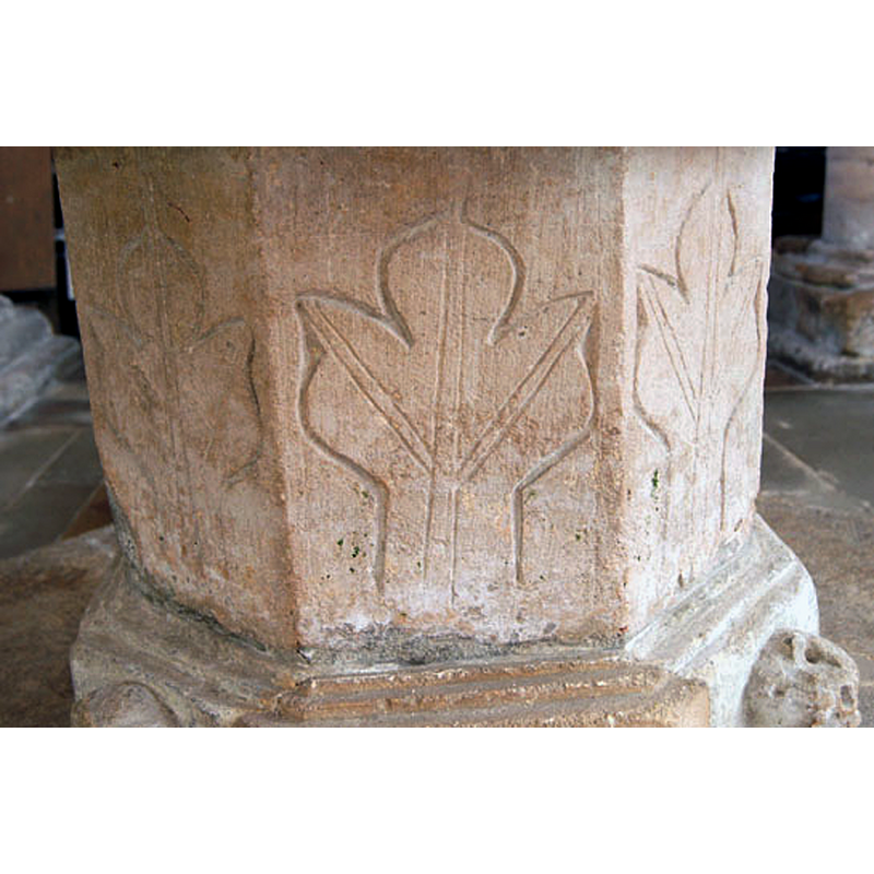Source caption: "The font rests on an octagonal pedestal with a curiously artless motif. It’s an apology for a design really and I can’t help wondering if it was some bodge-up from more recent times" -- large, oak?, on several sides of the stem of the base