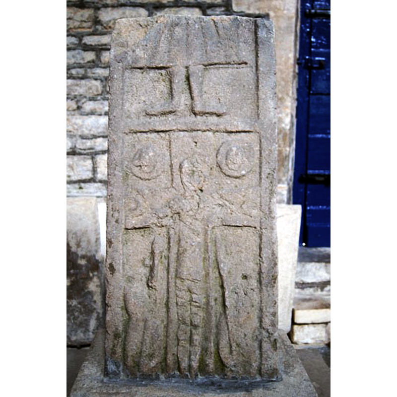 Source caption: "The c10 Anglo-Saxon cross shaft. There is a crucifixion scene at the bottom. To the left and right of Christ’s head are the sun and moon. Below the arms are two soldiers armed with lances."