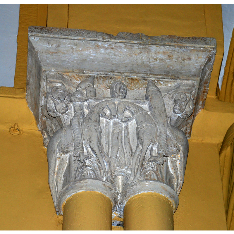 Source caption: "Capitel románico en la Iglesia de San Andrés en Revilla de Collazos (Palencia, Castilla y León). La pareja de capiteles que coronan las dobles columnas del triunfal estuvieron cubiertos, al igual que el pilar, por una fina capa de revoco con pintura imitando el veteado del mármol, circunstancia ésta que enmascaraba los detalles y dificulta su análisis estilístico. El correspondiente al lado de la epístola ofrece la representación de un tema relativamente frecuente en la escultura románica tardía, identificado como la Pax Dei y la Tregua Domini. La traducción plástica de dicha institución se concreta en una composición simétrica en la que dos caballeros, armados con casco cónico, cota de malla, escudo de tipo normando, espada al cinto y lanza en ristre, se aprestan a consumar su duelo mientras que un personaje mediador-en Revilla, como en buen número de casos, una mujer— detiene las monturas sujetándolas por las riendas. Dos cogollos completan la composición en los ángulos."
