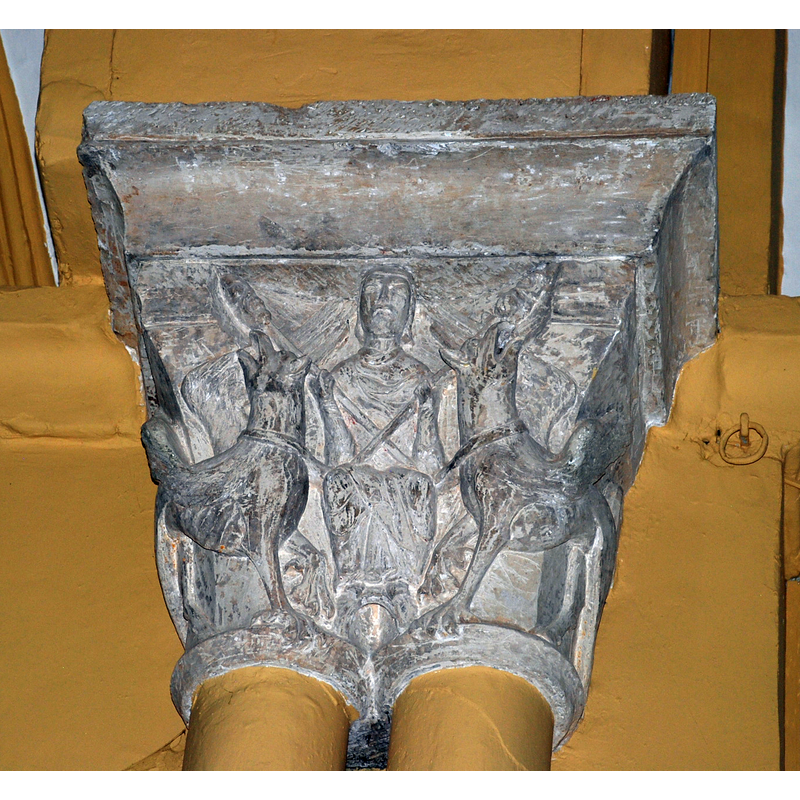 Source caption: "Capitel románico en la Iglesia de San Andrés en Revilla de Collazos (Palencia, Castilla y León). El capitel del lado del evangelio ilustra una Ascensión de Alejandro, escena ésta infrecuente en la plástica románica y cuya significación es polivalente. Según ésta, el monarca macedonio ascendió a los cielos arrastrado por dos grifos hambrientos que se elevaban persiguiendo en vano los trozos de carne ensartados en dos varas que el mismo Alejandro sostenía. En el relieve de Revilla vemos a Alejandro sentado sobre una cuerda que enlaza los cuellos de las bestias y sosteniendo las varas, cruzadas sobre su pecho, en las cuales se ensartan las piezas de carne que persiguen con sus picos los grifos. La visión frontal y majestuosa no deja de recordar las apoteosis imperiales romanas. La interpretación de la escena es delicada, ya que la figura de Alejandro fue considerada ya paradigma del héroe y modelo de gobernantes (y así en su ascensión podríamos ver una prefiguración de la de Cristo), ya ejemplificación de uno de los vicios más condenados en la Edad Media, como es la soberbia. En el caso concreto de Revilla el contexto mismo de la escena, frente a la imagen de la Pax Dei y su ubicación en el arco triunfal de la iglesia, y no en portadas o claustros como es habitual, nos decanta por su carácter positivo."