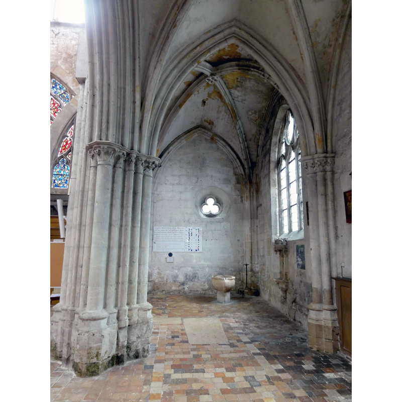 Source caption: "Moret-sur-Loing (77), église Notre-Dame, bas-côté nord, vue vers l'ouest" -- showing the baptismal font a the far end, and the wall-mounted piscina on the right, below the window