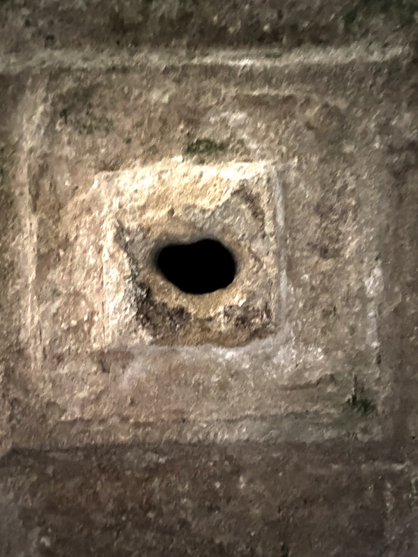 a hole made in the exterior of one of the basin sides; it would not be part of the original drainage of the font -- was it made when the font was re-purposed as a planter or similar use? [cf. FontNotes]