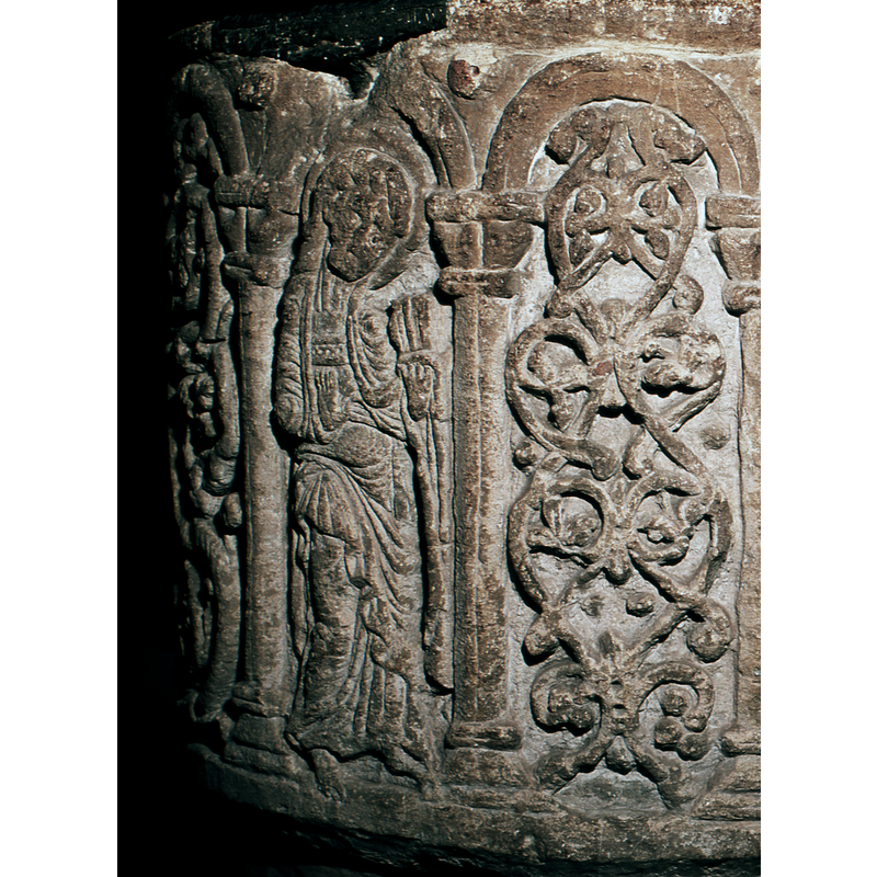 Tonsured figure carved on south-west side. He holds a fleur-de-lys or a key.