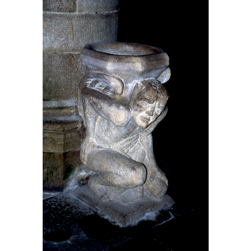 a grimacing demon holds up the holy-water stoup