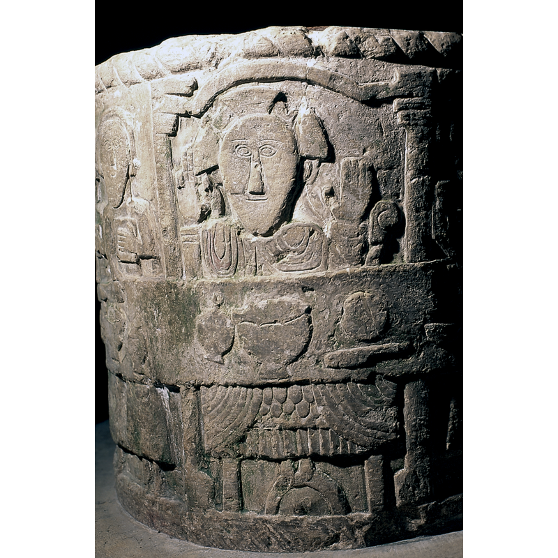 Last Supper. 12 apostles are present with Christ seated in the centre; Christ seats in his own space. framed by an arch supported on two columns; his hands are raised, the right in a blessing pose, the left in an orant pose; cruciferous nimbus [NB: the scene takes practically half of the surface of the font and is therefore impossible to photograph whole]