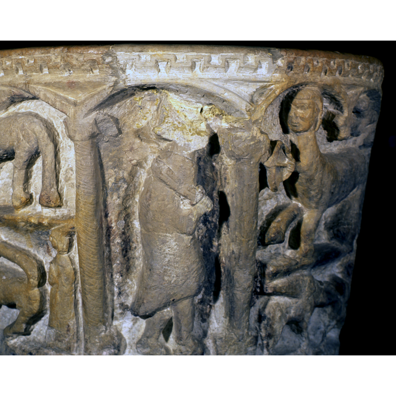 the upper part of this area has been damaged and repaired with a new carving of the arch-head and the Grecian fret at the upper rim, but there is hint of a hood on the head of the figure, which is an a passant to the right stance; the hood might suggest a cleric but the rest of the clothing and the sword do not; it is possible a half of a scene depicting a fight between this figure and the centaur in the next arch to the right, of which the front half is visible here pointing a tiny bow and arrow to the defaced figure -- partially visible in the previous arch, bottom left, is a human figure standing behing the rump of a lion