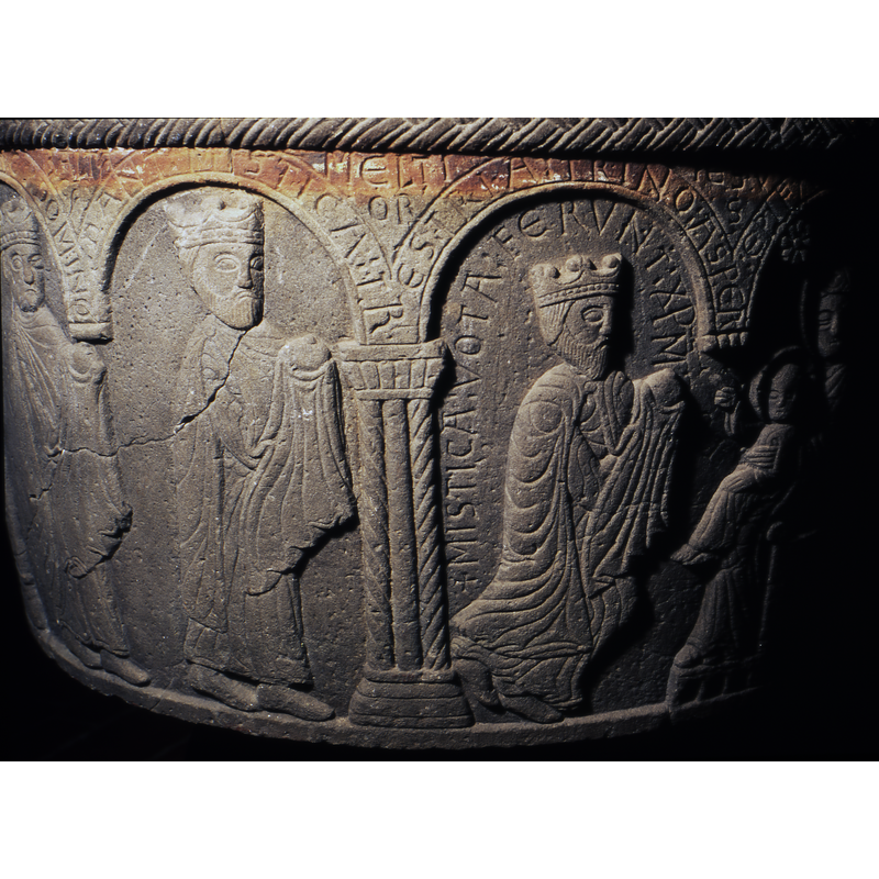 Adoration of magi. This takes place in two double arches. In the first double arch to the right, enthroned in profile is Mary with the Child. Her left arm holds the child on her knee, the child is haloed, cross in haloe, left arm rests on his knee and right arm raised in benediction toward the first magi. The first magi, in kneeling position, carried a gift on cloth covered hands. Is crowned and bearded. In the next arch, double arch, the first to the right, standing, in profile, dressed like the other. The last is similar to the previous one, but has no beard.