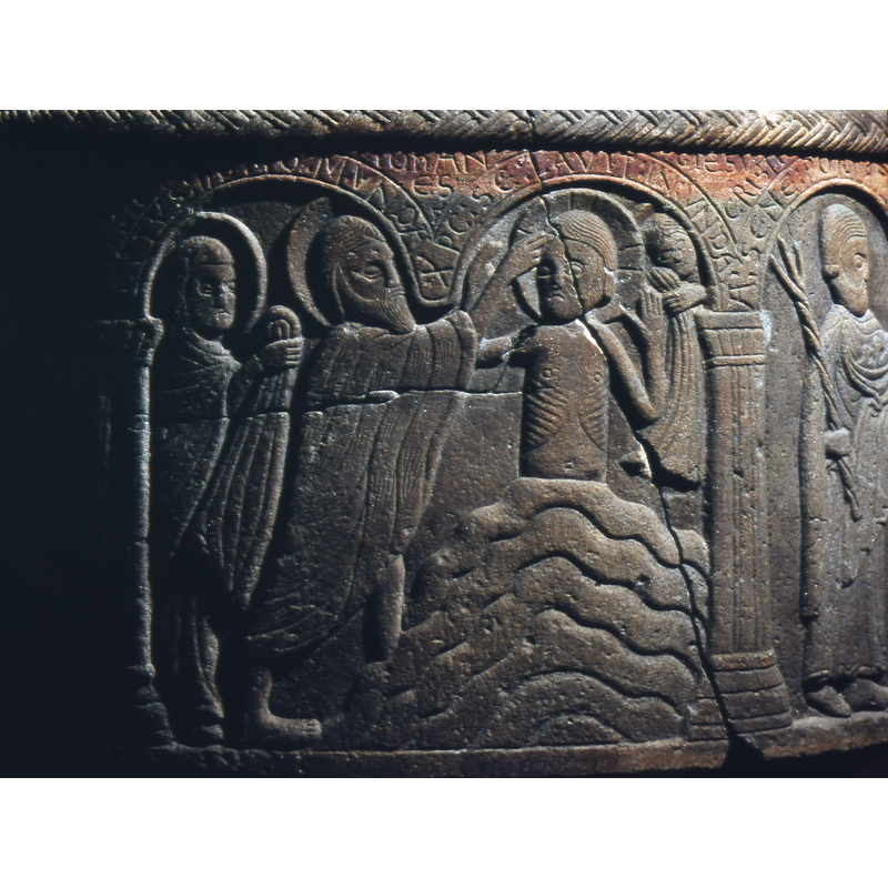 Baptism of Christ. In the middle of the first arch, to the right, Christ stands in the water up to his waist, is haloed, cross in haloe, and both palms are raised and open. At the top left corner a haloed figure, holds a cloth. This is probably an angel who would be typically part of such a scene. To the left of Christ, stands St.John, haloed, with a long animal skin cape over his back. Bare legs, right hand raised in benediction and raised to Christ's forehead. To the left behind John is Mary, haloed, head covered, and holding a cloth. This is the Virgin Mary. Nordstrom confirms this in his text, p. 99.