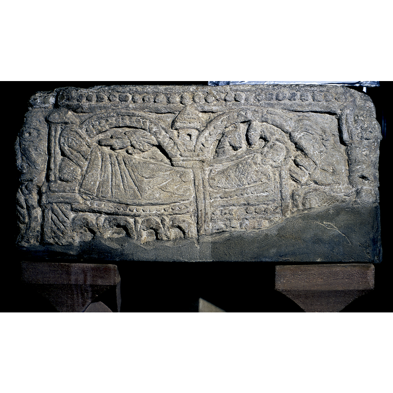 north side of the basin: the Virgin lies to the left with the hand of God coming over her; to the far right is seated Joseph watching over the child in the manger; the whole scene is framed in an architectural setting that includes two round arch-heads with beaded-tape pattern; in the spandrel of the two arches is a tower top and, the left arch-head rests on a tower-like edifice that is also the headboard of Mary's bed; as in many northern Nativity scenes, the bed is very elaborate, with torsade column and arcaded lower part; in this case the same decoration has been extended to tha manger in which the infant Christ lies. Joseph sits facing Mary and Christ, his head bowed and his hands in prayer. At the top of the scene, a row of bead motif, which also decorates the other sides of the basin. At the left and right angles are large heads with vegetation stemming from their mouths.