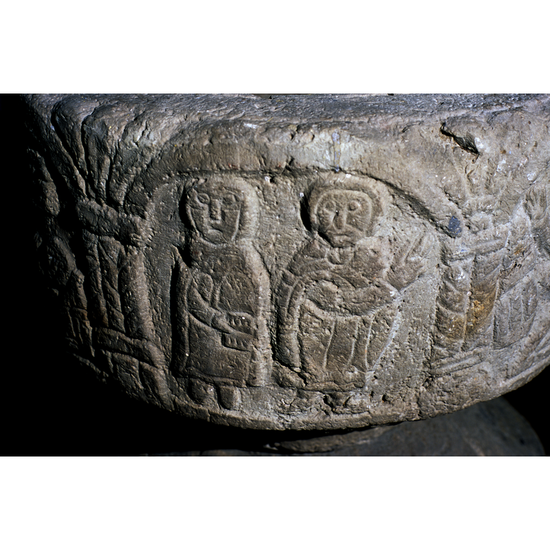 the cleric (?) on the left holds a book; the cleric (?) on the right points to the viewer's right; the scene in the next arch to the right  shows Christ in a chalice-shaped vessel
