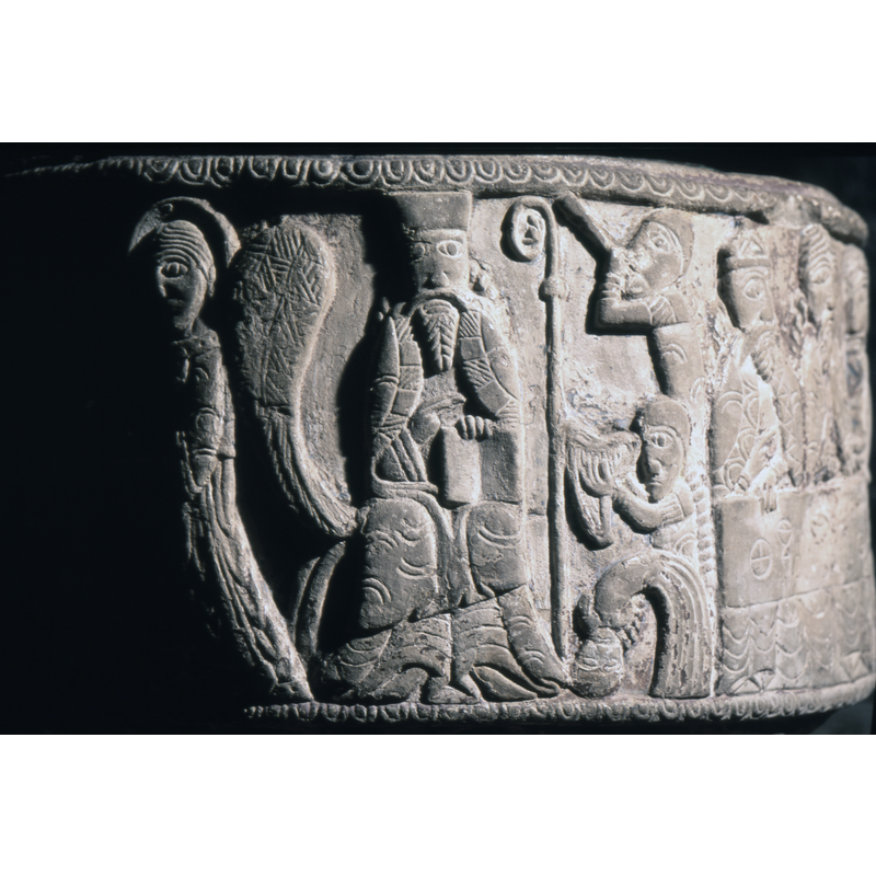 Enthroned figure with a free-standing bishop's staff to the right, right hand in benediction and the left hand holding open book. Two musicians to the right of the staff, the top playing flute or wind instrument and the lower one holding an Irish harp. There is a third figure bent over, with head touching ground.