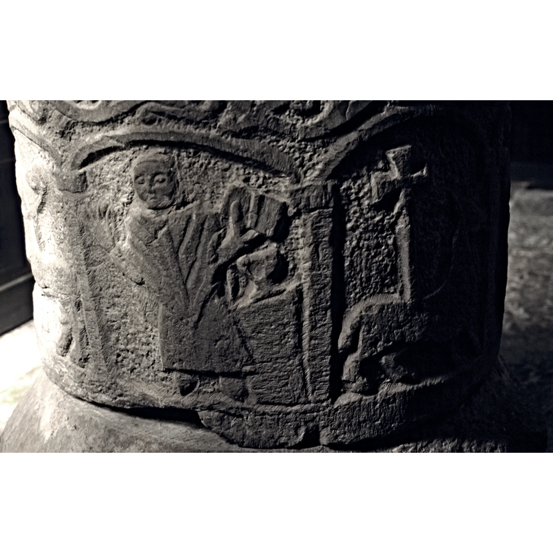 a cleric to the left of an altar with a chalice on it; the cleric holds an open book in his left hand