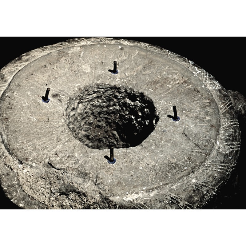 a top view of the surviving lower base of the font; the large hole in the centre was part of the drainage system, but the four pins are modern and they serve to secure the newly designed wooden block that supports the metal baptismal dish, also modern