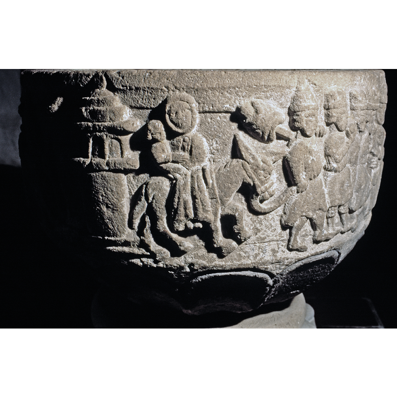no one is haloed in this scene; Mary wears a wimple and sits on the donkey facing the viewer, Christ child held in the crook of her right arm; Joseph wears a tiered hat similar to the one in his dream scene, and carries his bundle in a stick over his left shoulder; his right hand holds the donkey's lead