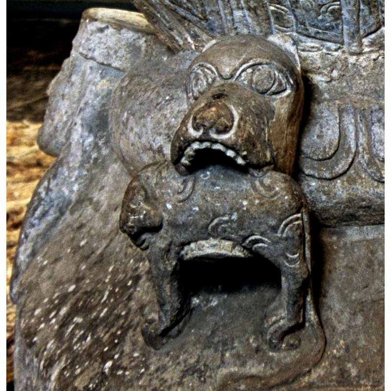 to the right of the human demi-figure; one of two large protruding animal heads with prey in their jaws; this one could perhaps be a bear or a dog