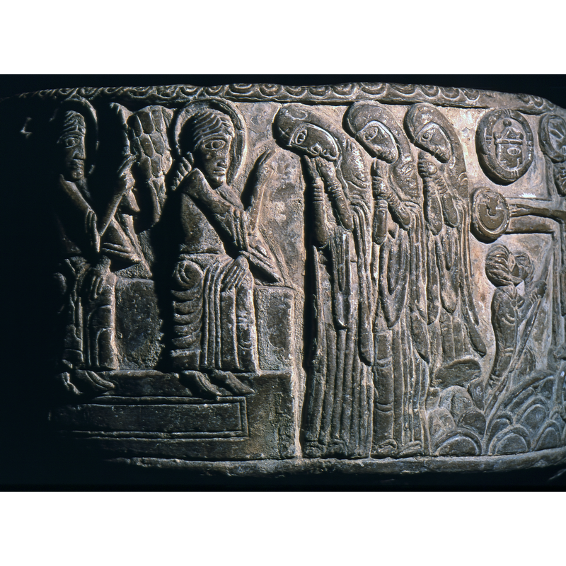 Three Marys at the Tomb, standing in profile facing to the left, all dressed in the same manner, heads bent. The first, on the left, rests her head on both hands and has a cross carved on the headdress; the two behind dressed in similar attire, holding their right wrists with their left hands. Two haloed angels sit on the rectangular tomb, giving benediction to the three Marys.