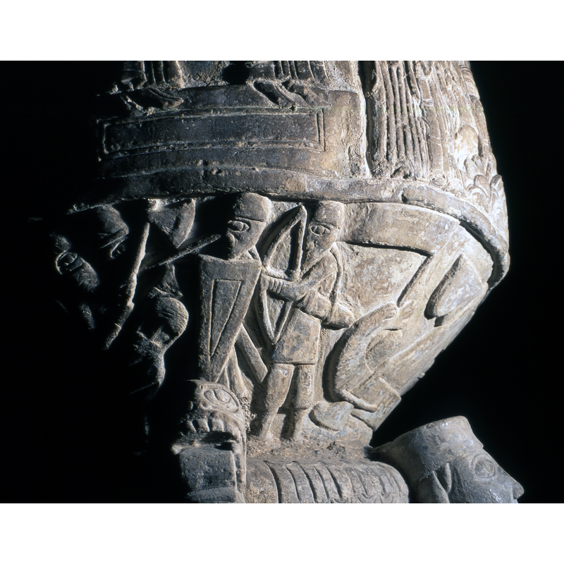 Battle scene [L -> R]: a warrior holds up a large ax over a falling soldier wearing chain-mail on his head; a soldier facing left is protected by a tall triangular shield; an archer faing left; at the extreme right the flag-bearing bow of a large ship
