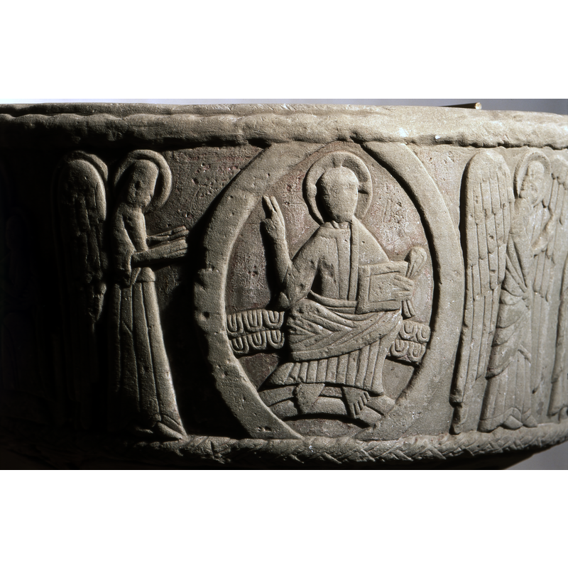 Christ in Majesty in the centre of a mandorla cross-haloed sitting on a patterned rainbow, his feet on a plain rainbow; he holds a book and a folded cloth in his left hand, the right hand raised in benediction; to the left of the mandorla is an angel in porfile, hands out but not touching the mandorla