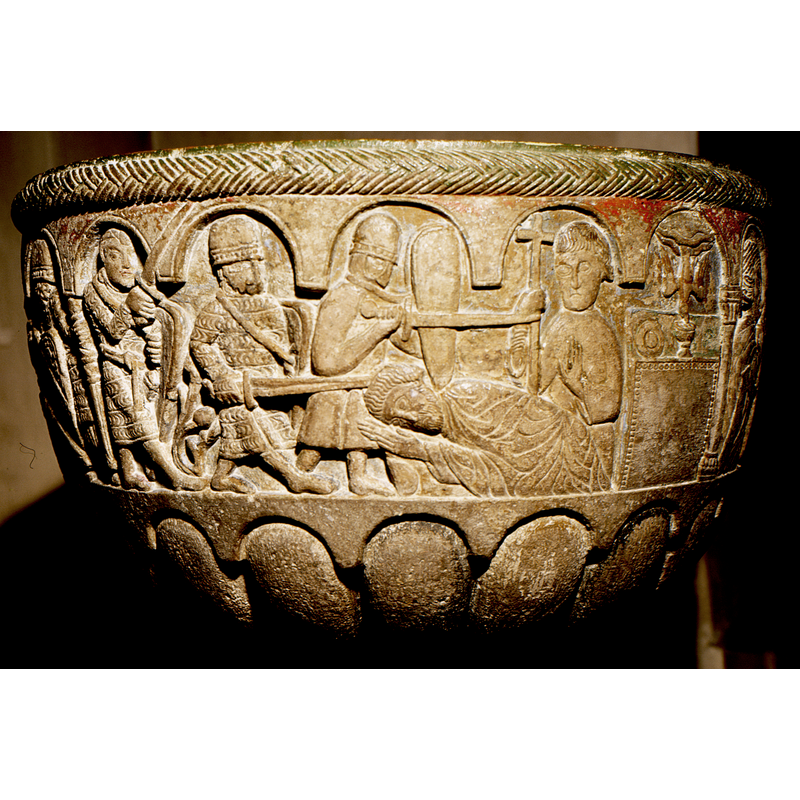 Murder of Thoms Becket. On the far right is the altar, chalice a dove with the hand of God  and a plate; to the left of the altar is a fiugre holding a cross in the right hand, the raised left hand in "stop" gesture; to the left is the lying figure of Thomas Beckett; his head is being hit by a sword from the second soldier on the left; there are three soldiers involved in this scene; the leftmost arch has the figure of the soldier who receives the execution order directly from the king