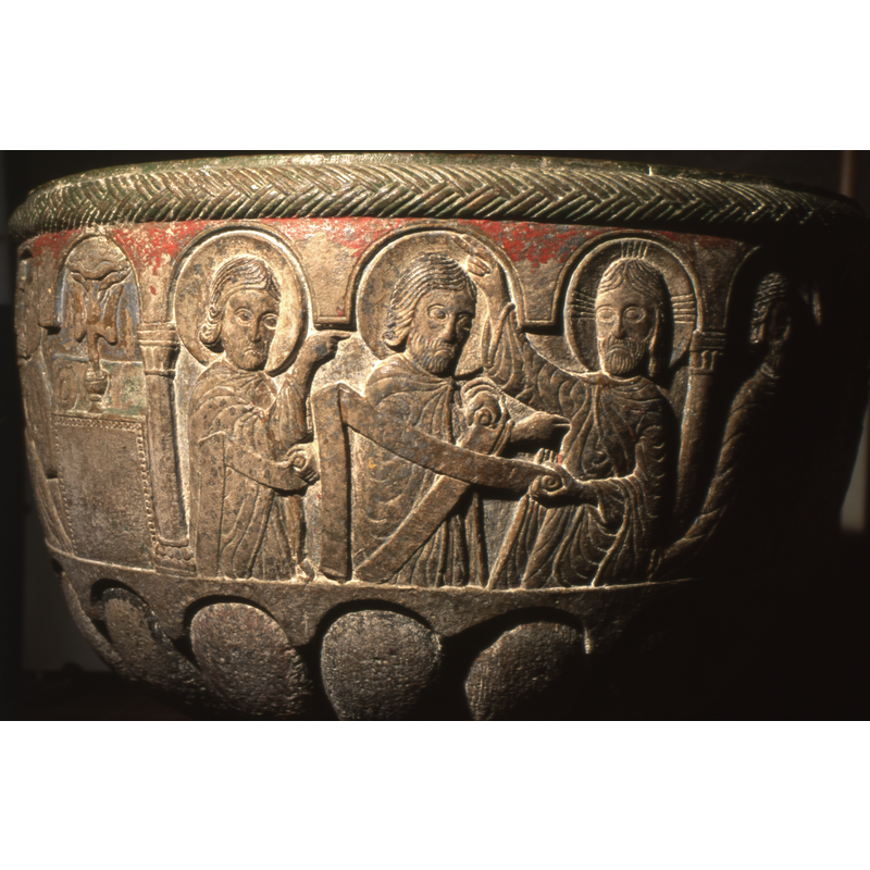 the scene contains hree figures framed by two columns; in the far right is Christ, with a cruciferous halo, is right hand raised in benediction while the left holds the end of a scroll; all the figures in this scene hold blank scrolls; the scrolls have no inscriptions carved on them, but may have had painted ones on them originally; the figure in the centre is bearded and wears a plain halo; is he the soul of Beckett?; the figure on the left is clean shaven and wears a plain halo; he points to the figure in the centre with the index finger of his right hand