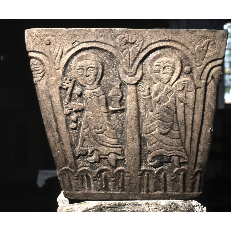 To the right of the main scene, there are two figures in arches. In the first, to the left, a figure, haloed, Saint Peter holds one key in the right hand and in the left hand holds a chalice shaped container or censor? There are three floating round dots carved in background. The next arch has an angel, right hand in benediction.