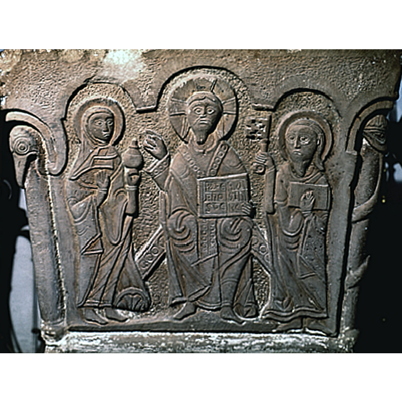 Christ in majesty. The is the central scene on this work. It takes up the whole one side of the font. In the centre of the composition sits, Christ, haloed, open book on his left knee and right hand in benediction.Firgure, to the left, is haloed, holding a container in left hand. It appears to be a woman with the type of headress she s wearing. To the right of Christ, is a bearded man, Saint Peter, with a key in his right hand and open book in his left.