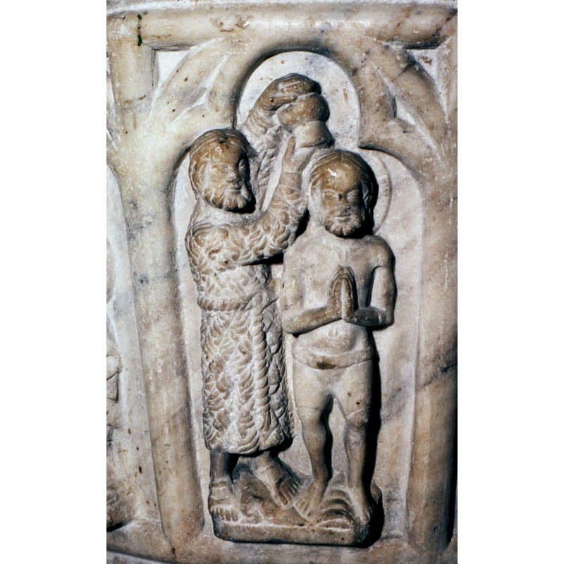 Haloed Christ stands with hands in orant position; feet on -rather than in- the water; John the Baptist, on the left, dressed in a skin garment tied with a cingulum, pores water on Christ's head from a pitcher