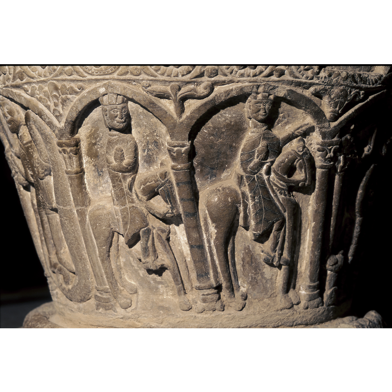 Adoration of the Magi. Under first arch to the far left, is a magi on horseback holding a gift in one hand. Under the second arch is a second Magi, on horseback, pointing toward the Madonna and Child. Under the third arch is a magi kneeling with a gift and you can see the head of his horse in the background. Under the fourth arch is the Madonna and Child. Under the fifth arch is Joseph who is standing holding the column with his right hand and a staff in his left hand