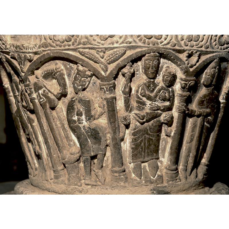 Adoration of the Magi. Under first arch to the far left, is a magus on horseback holding a gift in one hand. Under the second arch is a second Magus, on horseback, pointing toward the Madonna and Child. Under the third arch is a magus kneeling with a gift and you can see the head of his horse in the background. Under the fourth arch is the Madonna and Child. Under the fifth arch is Joseph who is standing holding the column with his right hand and a staff in his left hand