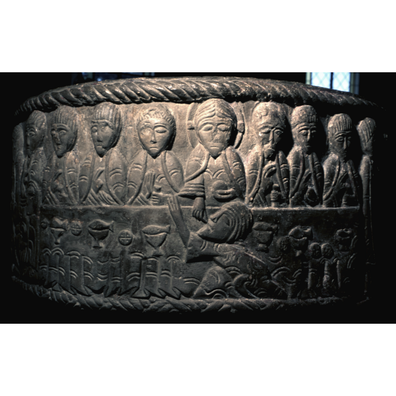 Last Supper. Large table dominates the scene. There are seven apostles present with Christ in the middle, full frontal, haloed with cross. In his left hand he holds a loaf of bread, and in his right hand, he feeds Judah over the table who is kneeling in the foreground. On the table there are loaves of bread with crosses, chalices with fish on top of the cups. To the left and right of Christ, three apostles on each side. Their right hands raised with two fingers in benediction - the left hand holds either bread or drinking vessel.