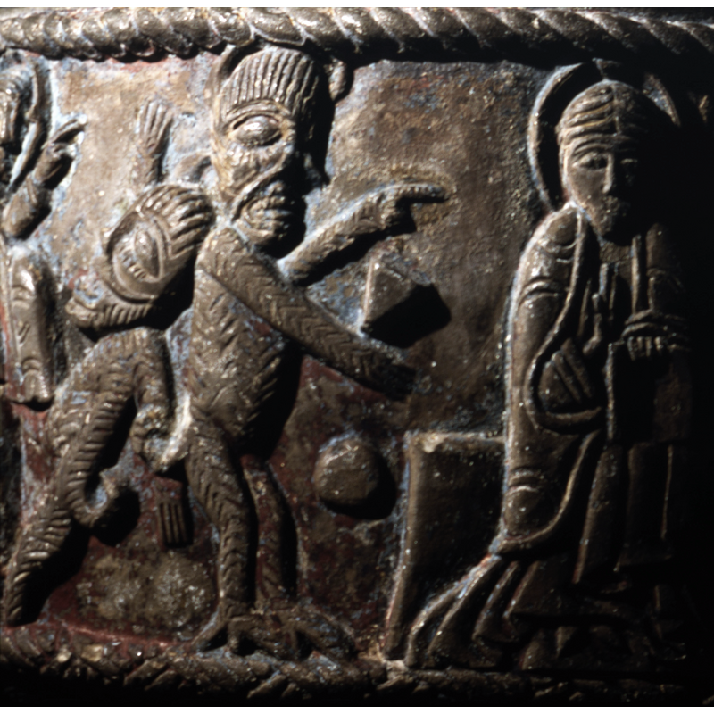 To the left, a large devil in profile, has tail, and claws, horns. To the right sits Jesus Christ, full front, haled, cross in haloe, right hand raised in benediction, left hand holds an open book.