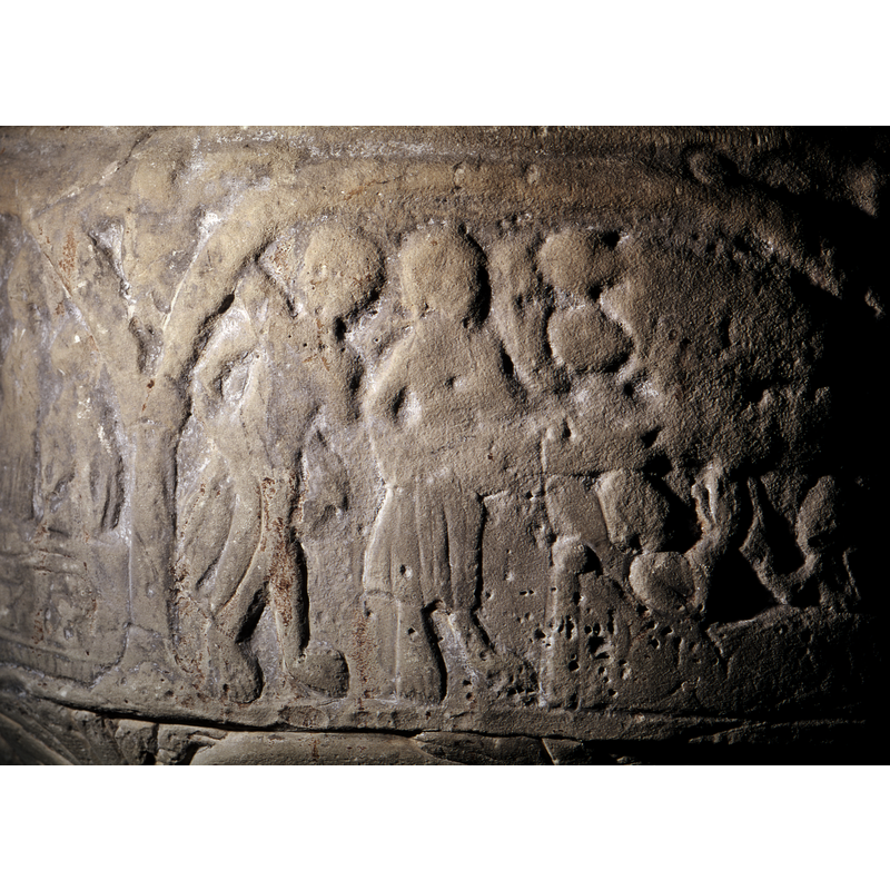 In the centre there is a standing figure with right hand raised and palm showing - benediction gesture? To the right on the lower part of the composition there is a rectangular object, table?, covered in cloth. There are three chalices on it; the lower part has pleats; above it, three figures; all badly worn. To the left of the centre figure the scene is divided by a rectangular frame - horizontal bar with two figures and below it again a rectangular shape - smaller. With one figure to the left of it and perhaps another to the right, although this is hard to tell; table has pleats. Could this be either the wedding at Cana or the Last Supper? Roosval (1918) suggests the Eucharist or Lord's Supper [="Abendmahl].