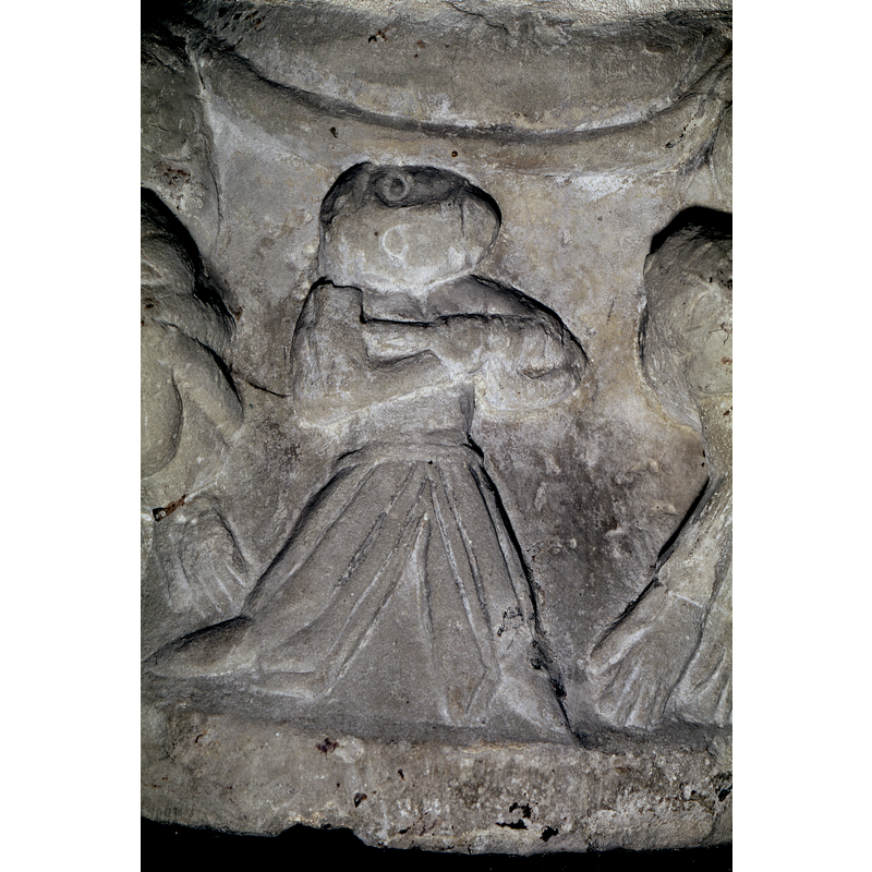 Figure standing with legs wide apart and wearing trousers; the arms hold a large hammer across the chest; the head is facing right and upward looking at the underbowl [NB: note that SK; Gotland, identifies as warrior about to slain a nearby beast]