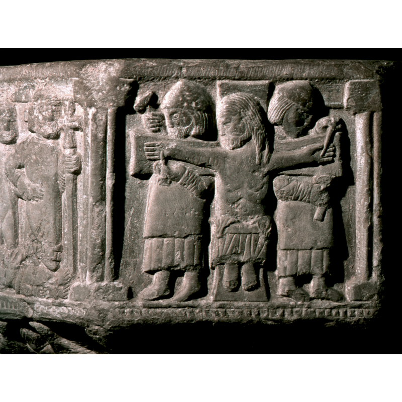 Crucificion to the left of Jesus's arrest and opposite the Nativity. In the centre, a large white cross, Jesus full front, naked to the waist, wears a lion cloth and his head is turned to the left - his hands are being nailed to the cross by two soldiers standing behind the cross.