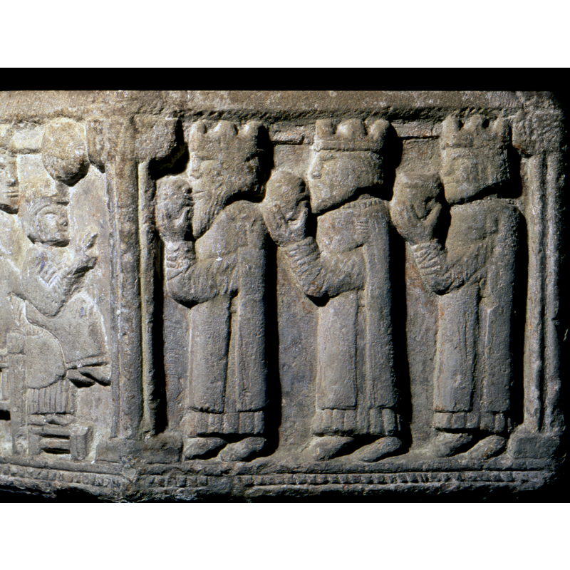 Adoration of the magi. Takes places over two sides. In the first side, a figure in profile, that looks like a priest, facing the Nativity. He wears a mantel, with a long cord around the neck and down the sides like a stole. The seated Madonna wears the same. To his right, is the Madonna and Child, both crowned, in profile, sitting on Gotland chair and feet rest on a stool. The child's hand is raised in benediction. To the right is a round star.ON THE NEXT SIDE three magi, profile, crowned, wearing capes, holding gifts and facing the left.