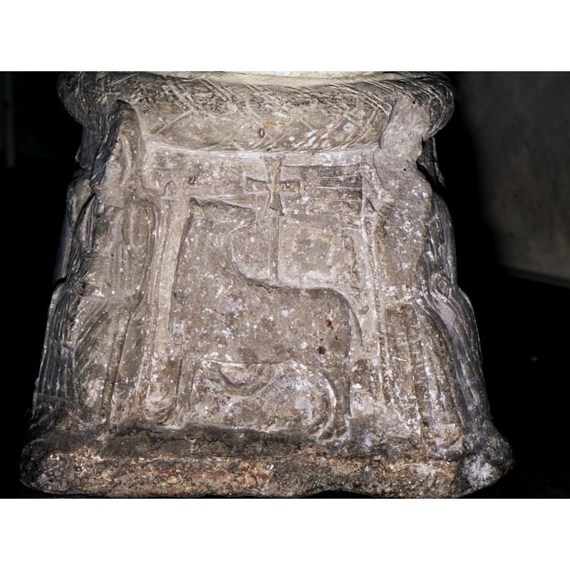 Lamb of God, facing left, head turned to the right. Holding cross in right paw. The cross has a large flag across the top.