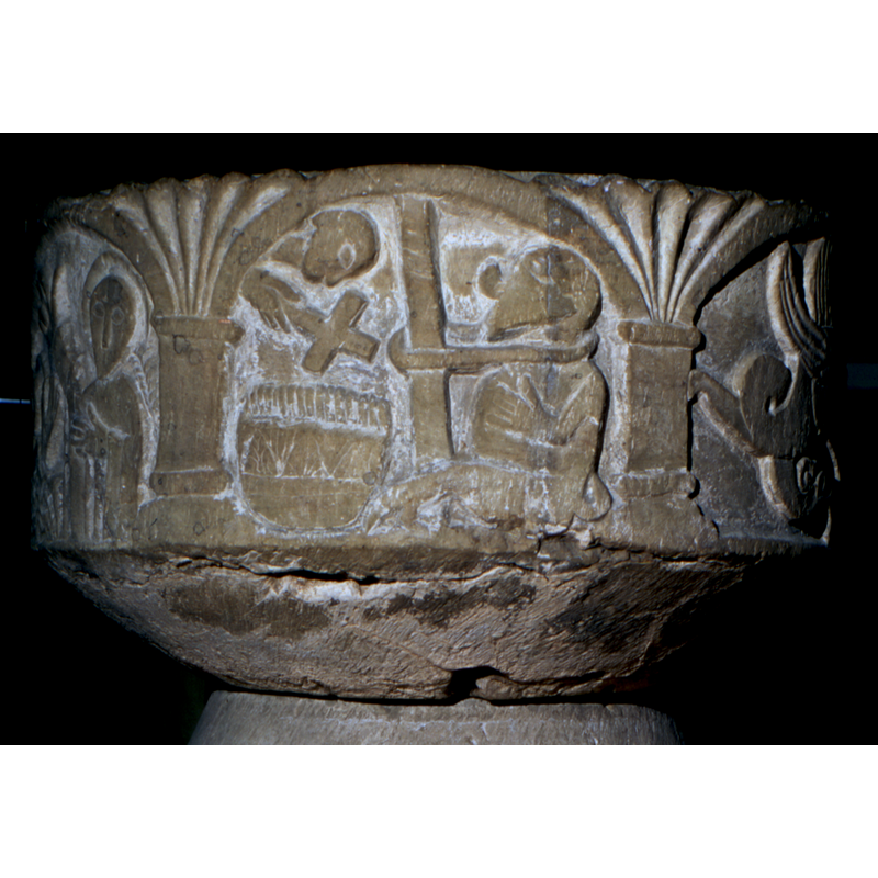 On the right side of the composition is the devil shown tied to a pole. A priest holds a cross over the water of the baptismal font, "Benedictio fontis". The font itself is cauldron-shaped and decorated vessel