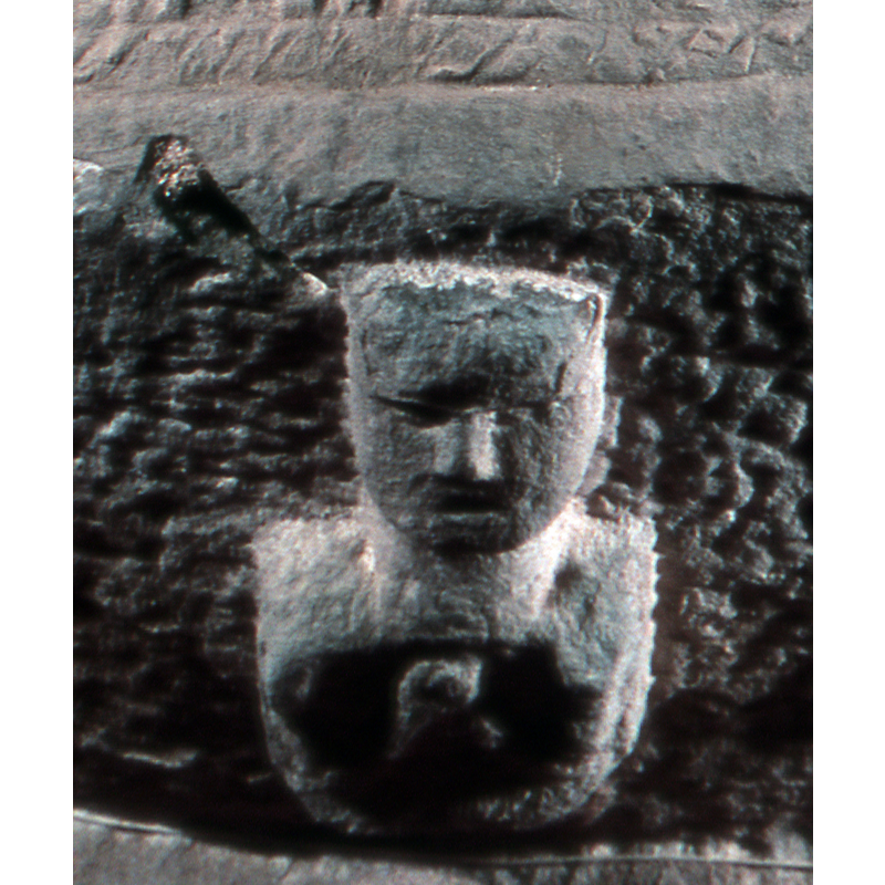 the bust is directly beneath the priestly figure on the basin side; it appears to have the arms folded and holding an object or a child
