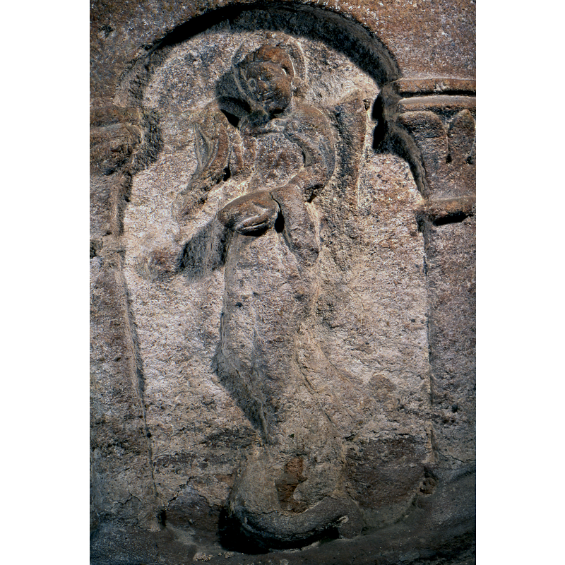 the haloed and winged figure is 3/4 turned to the left, an angel; the left hand appears to hold an object and has a cloth or maniple hanging from the wrist; there is a definite reptilian curved tail at the feet of the angel, which strongly siggests an identification as St. Michael